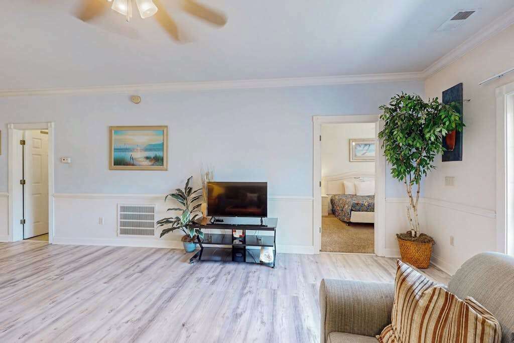 A spacious living room with a flat-screen TV on a stand, a large potted plant, and a door leading to another room.