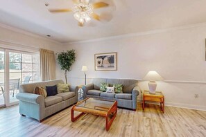 Ein geräumiges Wohnzimmer mit zwei Sofas, einem Couchtisch, einer Stehlampe und einem Deckenventilator.