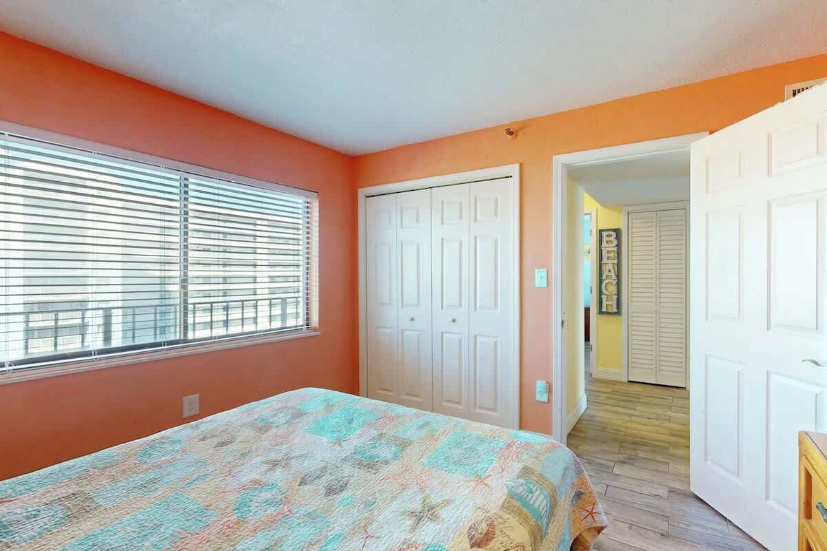 A bedroom with a bed, a window with blinds, a closet, and a door leading to another room.