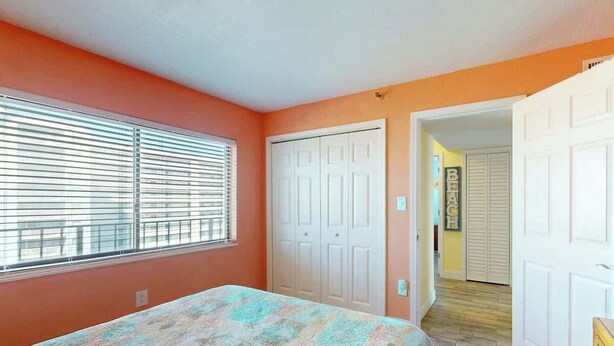 A bedroom with a bed, a window with blinds, a closet, and a door leading to another room. - Sea Winds PH4 Unit Condo (North Myrtle Beach)
