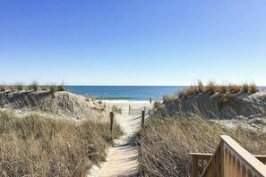 Ein sandiger Strandweg, der zum Meer führt, mit einem hölzernen Zaun an einer Seite.