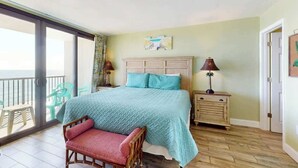 A bedroom with a bed, a chair, a nightstand, a lamp, and a view through a sliding door. - Sea Winds PH4 Unit Condo (North Myrtle Beach)