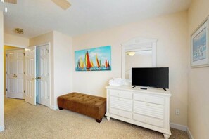 A room with a television on a white dresser, a painting of sailboats on the wall, and a brown bench. - Seaside Unit C Condo (Surfside Beach)
