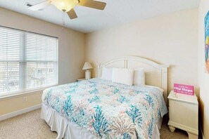 A bedroom with a bed, a nightstand, a ceiling fan, a window with blinds, and a wall with a sign. - Seaside Unit C Condo (Surfside Beach)