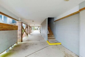 A corridor with a staircase leading to a garage, a brick pillar, and a concrete floor. - Seaside Unit C Condo (Surfside Beach)