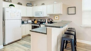 Una cocina moderna con armarios blancos, microondas integrado, estufa y una barra con taburetes.