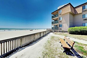 A beachfront property with a wooden walkway, a bench, and a building with balconies overlooking the ocean. - A Place at the Beach III 2-I (Myrtle Beach)