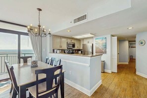 A modern kitchen with a central island, a dining area with a chandelier, and a view of the ocean. - Sand Dunes North Tower #1510 (Myrtle Beach)