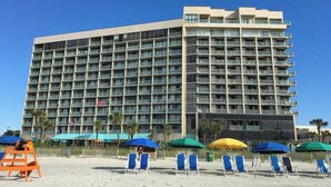 A multi-story hotel with a uniform facade, numerous balconies, and a beachside location with sun loungers and umbrellas. - Sand Dunes North Tower #1510 (Myrtle Beach)
