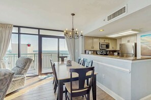 Eine moderne Küche mit einer zentralen Kochinsel, ein Essbereich mit einer Kronleuchter und Blick auf das Meer durch große Fenster.
