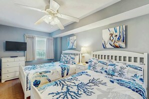 Ein Schlafzimmer mit zwei Betten, einem Deckenventilator, einem Fernseher und Bildern an der Wand.