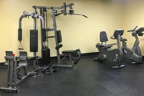 Ein Fitnessstudio mit unterschiedlichen Trainingsgeräten, darunter ein Multifunktionsgerät, eine Hantelbank und zwei Ergometer.