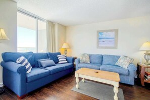 Ein Wohnzimmer mit zwei blauen Sofas, einem Holztisch und Meerblick durch große Fenster.