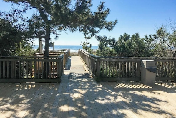 Eine Holzterrasse mit Geländern, die auf einen Strand hinausführt.