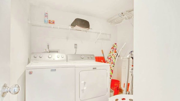 A laundry room with a front-loading washing machine, a dryer, a shelf with cleaning supplies, and a basket. - North Hampton Oceanfront 1501 (Myrtle Beach)