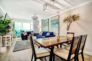 A dining area with a wooden table and chairs, a blue sofa, and a large plant. - Dunes Village Resort 1053 (Myrtle Beach)