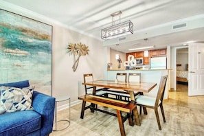 A dining area with a wooden table and chairs, a blue sofa, and a kitchen in the background. - Dunes Village Resort 1053 (Myrtle Beach)