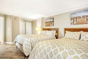 A hotel room with two beds, a wooden headboard, a lamp, and two paintings on the wall. - Dunes Village Resort 1053 (Myrtle Beach)