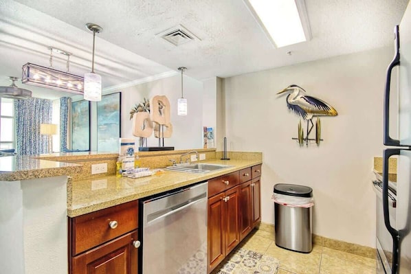 A kitchen with granite countertops, stainless steel appliances, wooden cabinets, and a trash can. - Dunes Village Resort 1053 (Myrtle Beach)