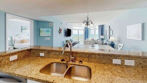 A modern kitchen with granite countertops, stainless steel sink, and a dining area with a chandelier. - Bay Watch Resort 0617 (North Myrtle Beach)