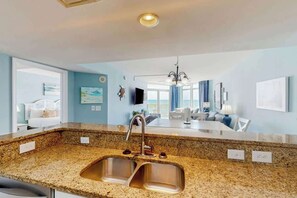 A modern kitchen with granite countertops, stainless steel sink, and a dining area with a chandelier. - Bay Watch Resort 0617 (North Myrtle Beach)