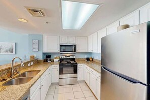 A modern kitchen with white cabinets, stainless steel appliances, and a granite countertop. - Bay Watch Resort 0617 (North Myrtle Beach)