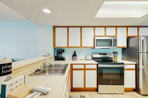 A compact kitchen with a microwave, stove, sink, and a refrigerator. - Roxanne Towers Unit 1101 (Myrtle Beach)