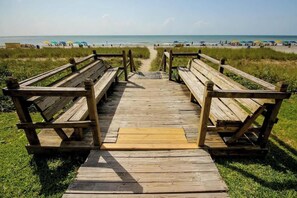 A wooden boardwalk leading to a beach with benches and umbrellas. - Roxanne Towers Unit 1101 (Myrtle Beach)