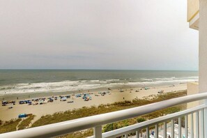 A beach view from a balcony with a railing, ocean, and beachgoers. - Bay Watch Resort 0834 (North Myrtle Beach)