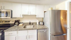 Una cocina con gabinetes blancos, un refrigerador de acero inoxidable, un microondas, una estufa, un fregadero y un tostador.