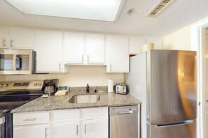 A kitchen with white cabinets, a stainless steel refrigerator, a microwave, a stove, a sink, and a toaster. - Bay Watch Resort 0834 (North Myrtle Beach)