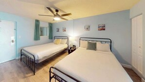 Una habitación con dos camas, un ventilador de techo y una puerta.