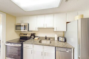 A compact kitchen with white cabinets, a microwave, a stove, a sink, a toaster, and a dishwasher. - Bay Watch Resort 0834 (North Myrtle Beach)