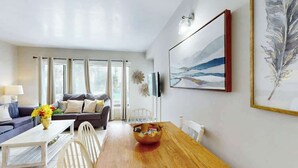 Un salon moderne avec une table à manger en bois, un ensemble de canapés et un grand tableau accroché au mur.