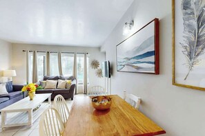 A modern living room with a wooden dining table, a sofa set, and a large painting on the wall. - Palace Resort Unit 108 (Myrtle Beach)