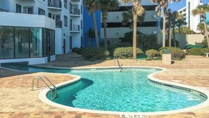 Une piscine dotée d’une terrasse carrelée, entourée de palmiers et de bâtiments modernes.