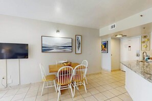 A modern kitchen with a dining area, featuring a flat-screen TV, a large painting, and a decorative wall piece. - Palace Resort Unit 108 (Myrtle Beach)