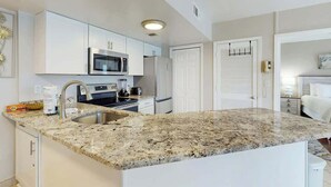 Une cuisine moderne avec des meubles blancs, un plan de travail en granit, des appareils électroménagers en acier inoxydable et un four encastré.