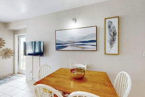 A dining area with a wooden table, white chairs, a TV, and framed artwork on the wall. - Palace Resort Unit 108 (Myrtle Beach)