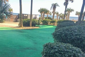 A golf course with a green fairway, palm trees, and a building in the background. - Palace Resort Unit 108 (Myrtle Beach)