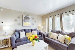 A living room with two grey sofas, a white coffee table, and a vase of yellow flowers. - Palace Resort Unit 108 (Myrtle Beach)