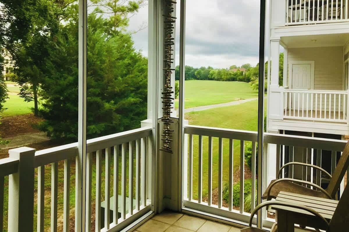 A balcony with a view of a green landscape, a white railing, and a door.