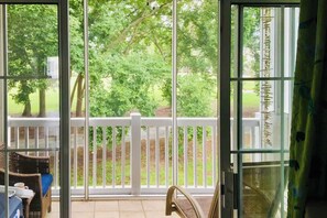 A room with a view of a garden through a glass door, a white railing, and a wicker chair. - Barefoot Sun & Golfing Fun (North Myrtle Beach)