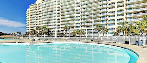 A large hotel with multiple balconies, a swimming pool, and palm trees.