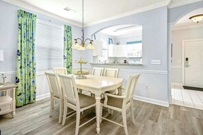 A dining area with a round table, six chairs, and a chandelier. - Barefoot Sun & Golfing Fun (North Myrtle Beach)