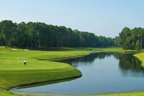 A golf course with a pond, surrounded by trees. - Barefoot Sun & Golfing Fun (North Myrtle Beach)