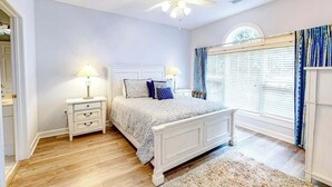Una camera da letto con un letto, comodini, una ventola a soffitto, una finestra con tende e una porta.