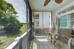 A balcony with a view of a green landscape, a white railing, and two wicker chairs. - Barefoot Sun & Golfing Fun (North Myrtle Beach)