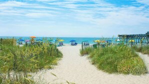 Un sentiero sulla spiaggia che conduce a ombrelloni e lettini.