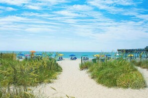 Ein Weg am Strand zu Strandliegen und Sonnenschirmen.